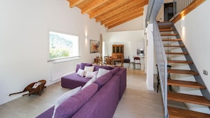 A spacious living room with a purple sofa, a wooden staircase, and a view of the kitchen. - Villa Sasseta - Eight Bedroom Villa, Sleeps 16 (Zignago)