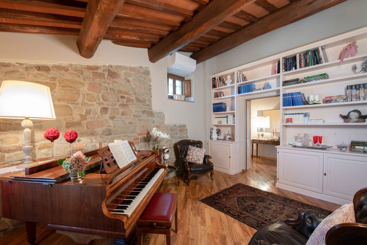 Un accogliente soggiorno con un pianoforte a coda, un caminetto e una libreria piena di libri e oggetti decorativi.