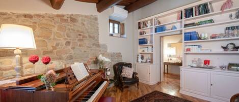 Un accogliente soggiorno con un pianoforte a coda, un caminetto e una libreria piena di libri e oggetti decorativi.