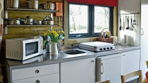 A kitchen with wooden walls, a window with a red curtain, stainless steel appliances, and a variety of pots and pans on shelves. - Kestrel Cabin - UK1246 (Brocklebank, near Caldbeck and Uldale)