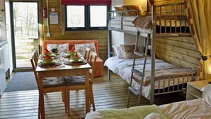 A wooden cabin with bunk beds, a dining table set with plates and glasses, and a view through a window. - Kestrel Cabin - UK1246 (Brocklebank, near Caldbeck and Uldale)