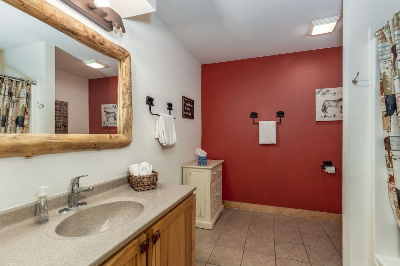 Un baño con un espejo grande, un lavamanos, un armario y una pared roja.