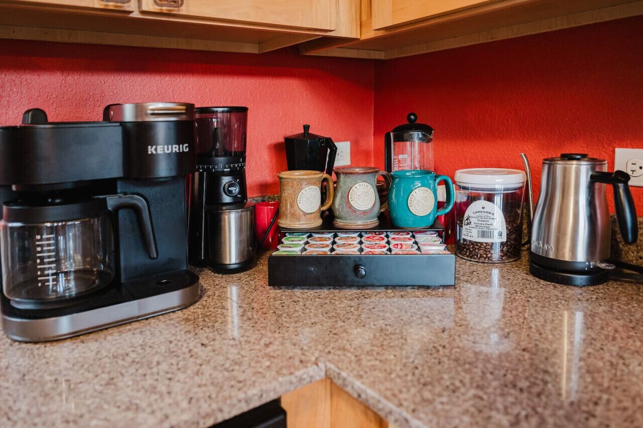 Uma cozinha com cafeteira, liquidificador, moedor de café e jarra de café na bancada.