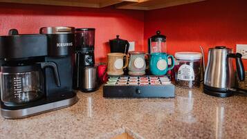 Uma cozinha com cafeteira, liquidificador, moedor de café e jarra de café na bancada.