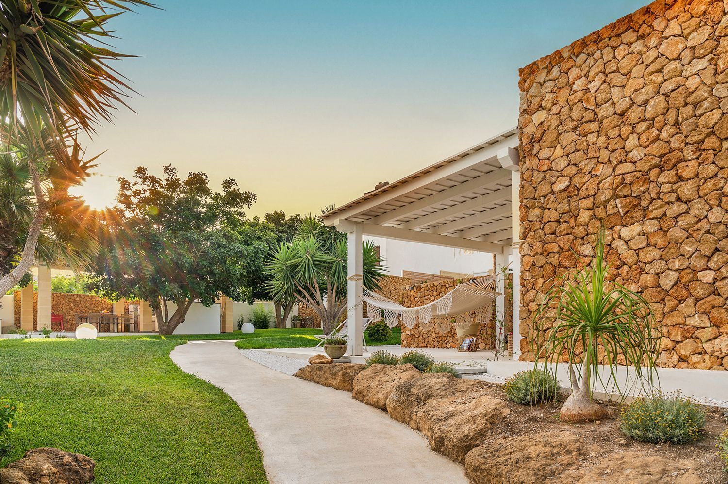 A modern outdoor patio with a stone wall, a covered seating area, and a well-maintained garden.