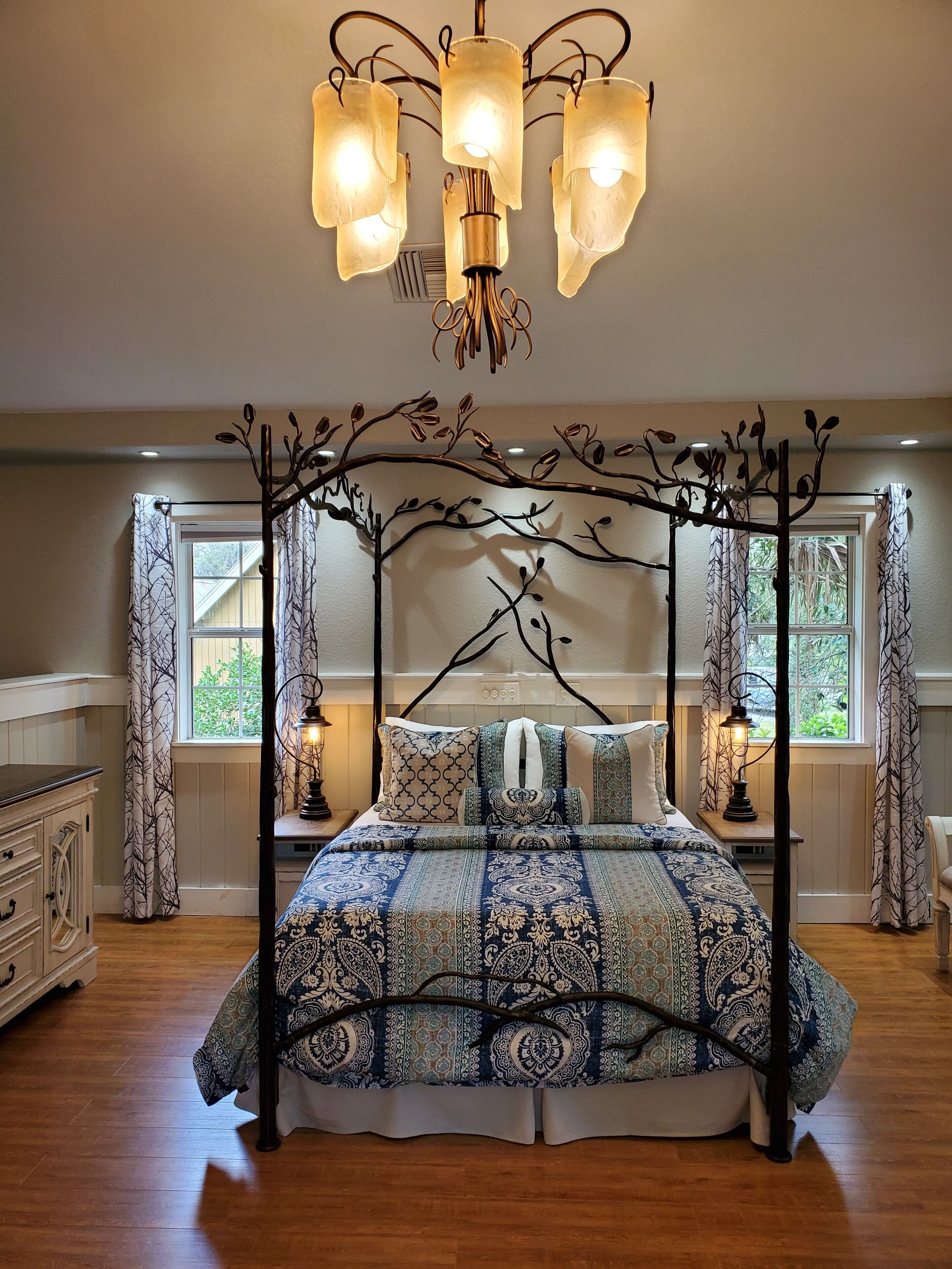 A bedroom with a four-poster bed, patterned bedding, a chandelier, and a decorative tree branch ceiling design.
