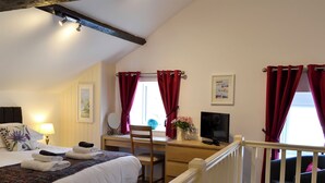 Quarto de hotel com uma cama, uma escrivaninha com computador, uma cadeira, uma janela com cortinas vermelhas e uma escada.