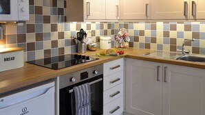 Cozinha moderna com micro-ondas, forno e pia. Possui armários, painel de azulejos e diversos utensílios de cozinha.