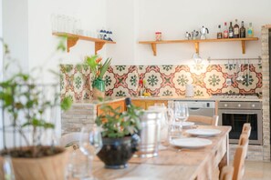 Cucina con parete in mattoni, mensole in legno e tavolo imbandito per sei persone.