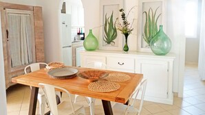 A dining area with a wooden table, white chairs, and a kitchen in the background. - Villa Minni - Three Bedroom Villa, Sleeps 6 (Monacizzo-librari-truglione)