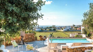 A poolside area with stone walls, outdoor furniture, and a view of the sea and buildings in the distance. - Villa Minni - Three Bedroom Villa, Sleeps 6 (Monacizzo-librari-truglione)