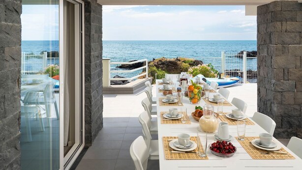 A dining area with a view of the sea, stone walls, and a table set for a meal. - Villa Sul Mare - Eight Bedroom Villa, Sleeps 16 (Acireale)