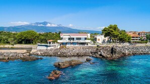 A coastal property with a large house featuring a balcony and a pool, situated near clear blue waters and rocky outcrops. - Villa Sul Mare - Eight Bedroom Villa, Sleeps 16 (Acireale)
