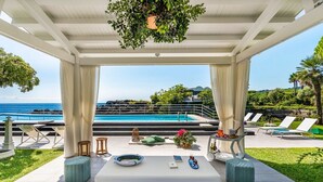A covered outdoor seating area with a pool view, cushioned seating, and a small table with drinks. - Villa Sul Mare - Eight Bedroom Villa, Sleeps 16 (Acireale)