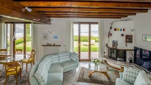 A cozy living room with a sofa, a dining table, and chairs. There is a fireplace and a television. - Villa Meina - Four Bedroom Villa, Sleeps 8 (Meina)