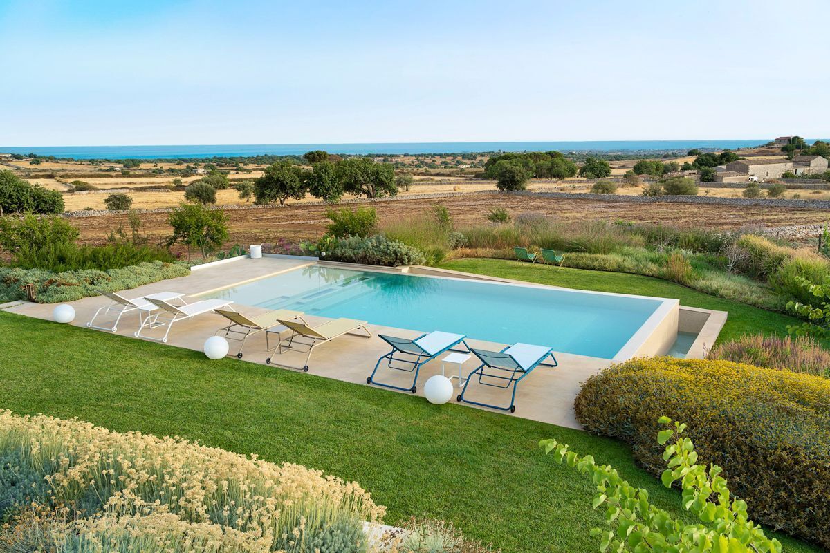 Une piscine rectangulaire à l’eau d’un bleu limpide, entourée d’une pelouse bien entretenue et d’une variété de plantes.