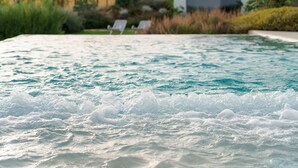 A pool with water gently lapping against the edge, surrounded by a landscaped garden with various plants and a modern building in the background. - Villa Suprema - Four Bedroom Villa, Sleeps 8 (Pirato)