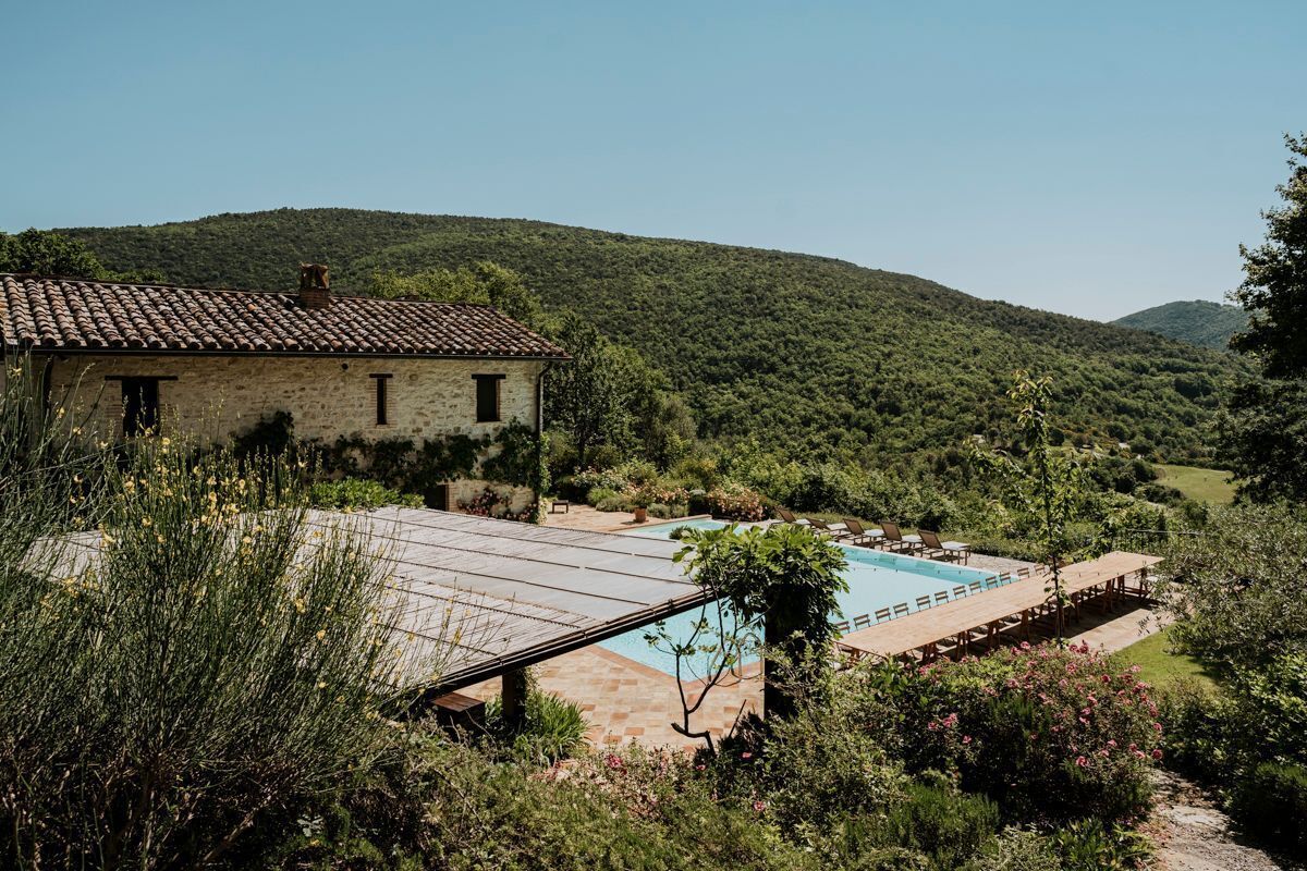 Un bâtiment en pierre doté d’une piscine et d’un espace extérieur aménagé, entouré d’une végétation luxuriante et de collines.