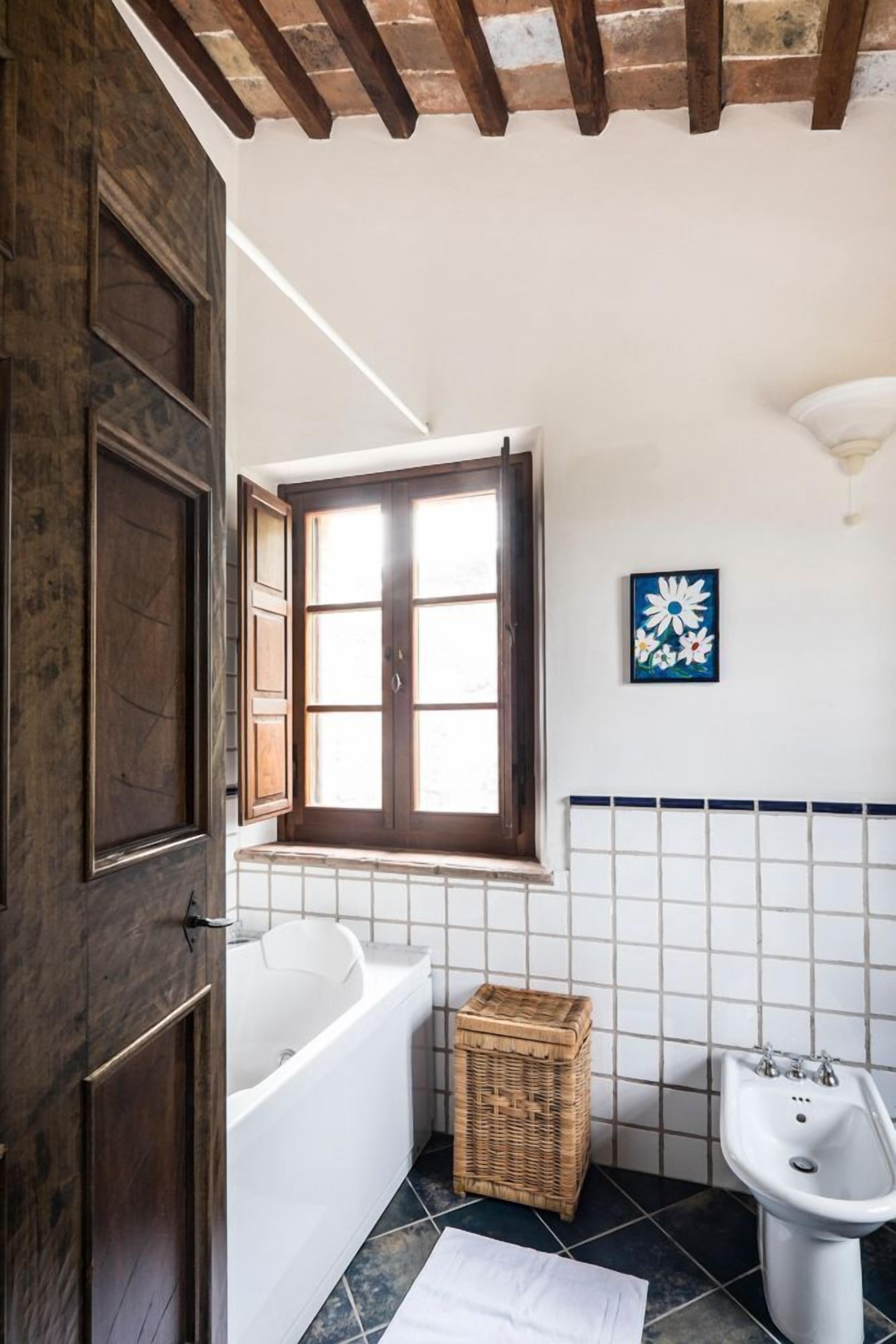 A bathroom with a bathtub, a bidet, a window, and a decorative wall piece.