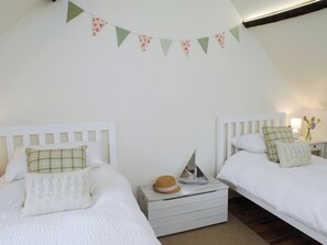 A bedroom with two beds, a nightstand, a hat, and a decorative string of triangular flags.