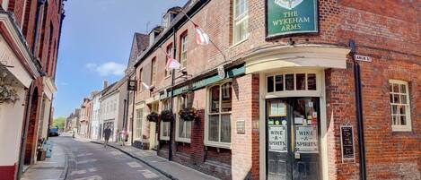 A traditional brick building with a sign for 'The Wykeham Arms' pub, a cobblestone street, and a clear blue sky.