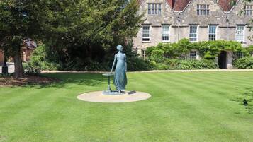 Une statue se dresse sur une pelouse parfaitement entretenue, avec un bâtiment en pierre en arrière-plan.