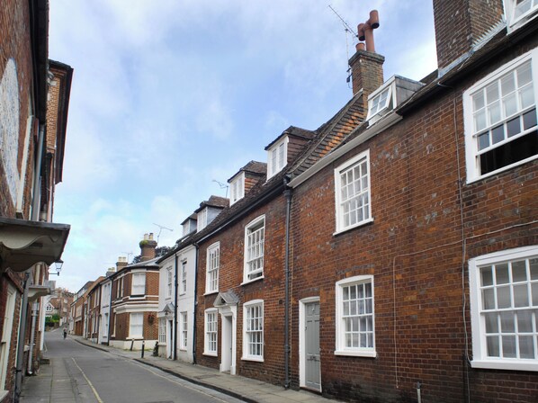 A row of traditional brick townhouses with white-framed windows and doors, a clear sky, and a quiet street. - 2 bedroom accommodation in Winchester (Winchester)