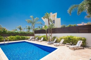 Ein Pool mit Liegestühlen, Palmen und einem modernen Gebäude im Hintergrund.