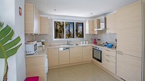 Una cocina moderna con armarios de madera clara, una isla central, horno integrado y una ventana con vistas a zonas verdes.