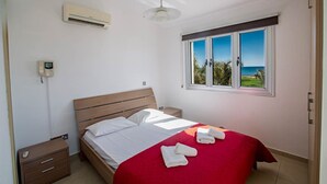 Un dormitorio con cama, mesita de noche, aire acondicionado de pared, ventana con vistas y una lámpara en el techo.
