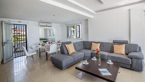 Una sala de estar moderna con un sofá seccional gris, una mesa de comedor y una cocina visible a través de una puerta abierta.