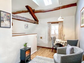 Ein gemütlicher Raum mit Kamin, Holzbalken, einem Esstisch mit Stühlen und einem Fenster mit Vorhängen.