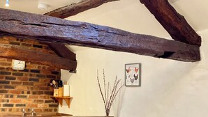 A rustic kitchen with exposed wooden beams, a brick wall, and a wall-mounted clock. - Rebecca Puddle Duck Cottage (Bassenthwaite)