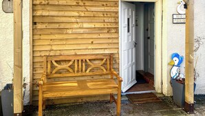 A wooden bench outside a building with a white door, a wooden pergola, and a bird-shaped decoration. - Rebecca Puddle Duck Cottage (Bassenthwaite)