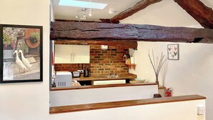 A kitchen with exposed wooden beams, a brick wall, a white countertop, and a hanging light fixture. - Rebecca Puddle Duck Cottage (Bassenthwaite)