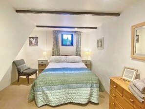 Une chambre à coucher comprenant un lit, deux tables de chevet avec des lampes, une chaise, une commode et une fenêtre avec des rideaux.