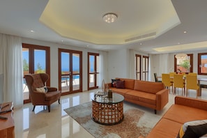 A spacious living room with a large sofa, a coffee table, and a dining area with yellow chairs.