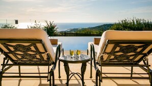A patio with two lounge chairs facing a pool and ocean view. - Aphrodite Hills Resort - 4 Bedroom Mythos Collection Villa I (Kouklia)