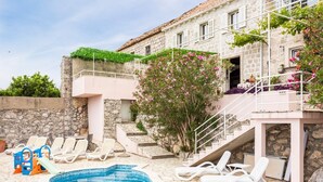 Un espace piscine avec des chaises longues, un petit toboggan et un bâtiment en pierre doté d’un balcon.