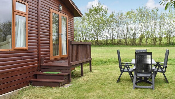 A wooden cabin with a deck, a satellite dish, and a table with chairs outside. - 3 bedroom accommodation in Lanreath, near Looe (Lanreath, near Looe)