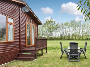 Une cabane en bois avec une terrasse, une antenne parabolique et une table avec des chaises à l’extérieur.