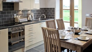 A modern kitchen with a dining area, featuring a large window, built-in oven, and a coffee maker. - 3 bedroom accommodation in Ystrad Meurig (Ystrad Meurig)