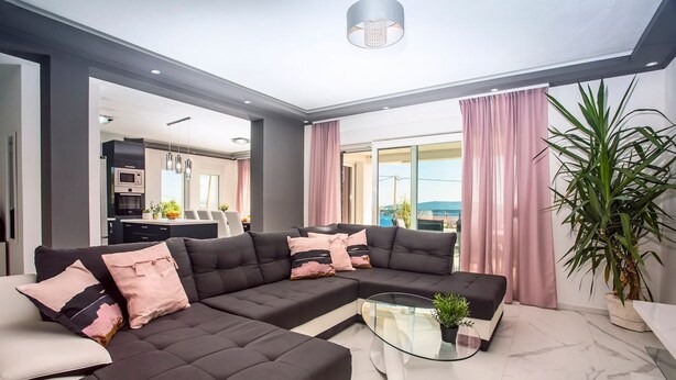 Ein modernes Wohnzimmer mit einem Ecksofa, einem Glastisch und Blick ins Freie.