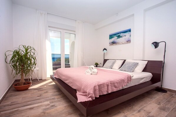 Un dormitorio con cama, una planta en maceta, un cuadro y vista al mar.