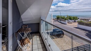 A balcony with a view of the sea, a parked car, and a table with chairs.
