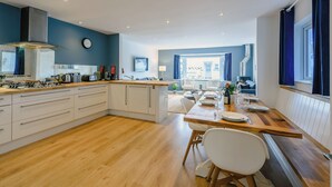 A modern kitchen with a central island, dining area with chairs, and a view of the street.