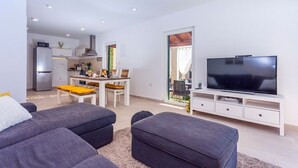 A modern living room with a flat-screen TV, grey sofas, and a dining area with a table and chairs.