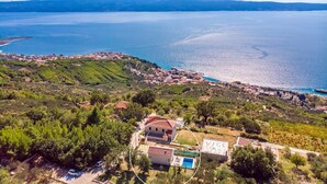 A coastal village with a prominent house surrounded by greenery and a clear view of the sea.
