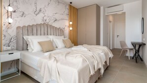 Une chambre moderne avec un mur à motifs de marbre, un lit doté d’une tête de lit beige, des tables de chevet et un petit bureau avec une chaise.