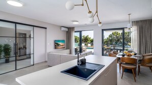 Une cuisine moderne dotée d’un îlot central, d’un coin repas avec des chaises en bois et de grandes fenêtres offrant une vue sur l’extérieur.